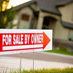 Brown and beige house in the background with red a white for sale by owner sign with a red arrow pointing towards the house.