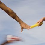 two runners in red running uniform handing eachother a yellow Bataan