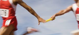 two runners in red running uniform handing eachother a yellow Bataan